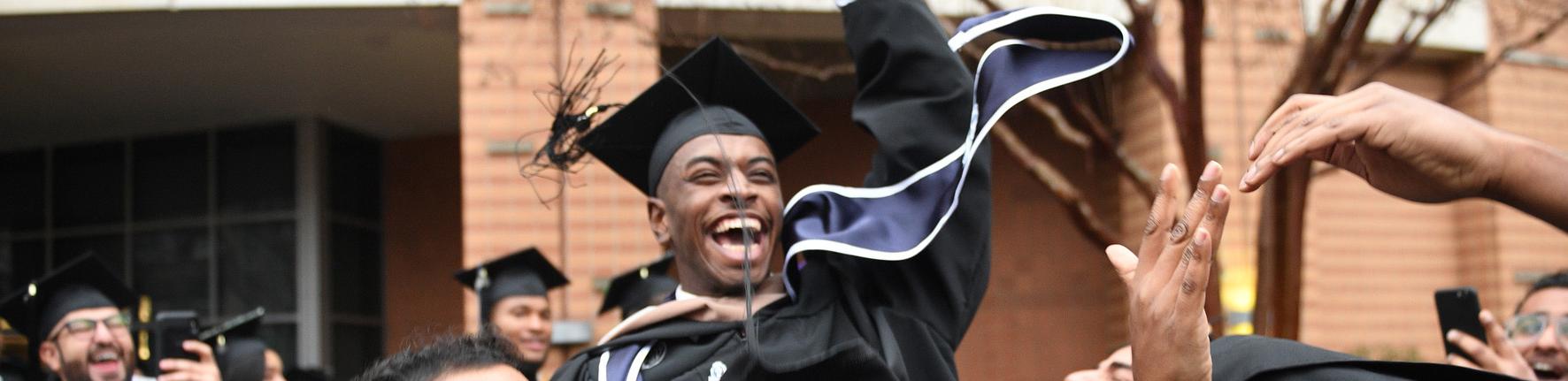 研究生 laughs as he is lifted up by his fellow graduates