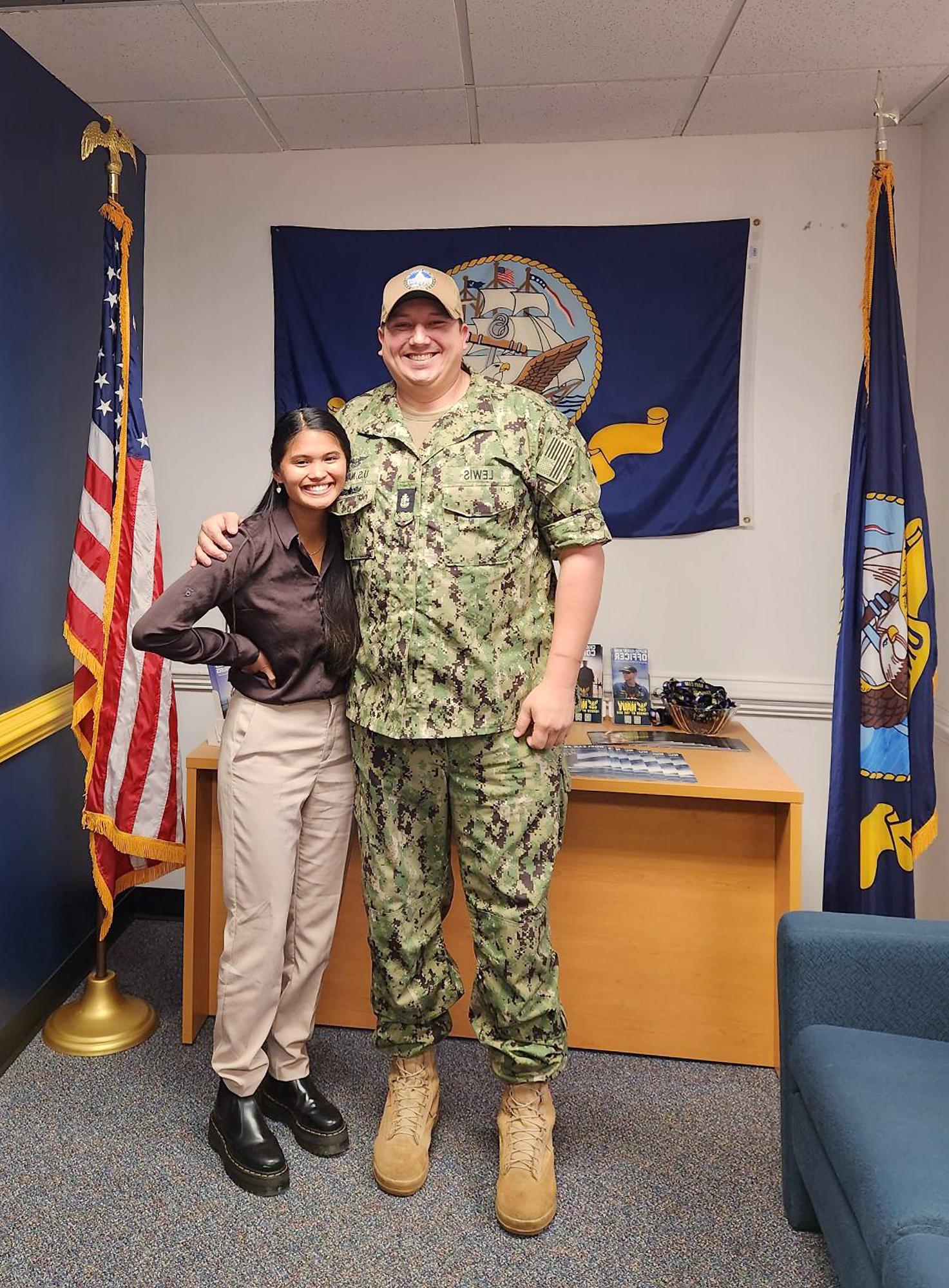 Tall man in a military uniform stands with woman in recruiting office