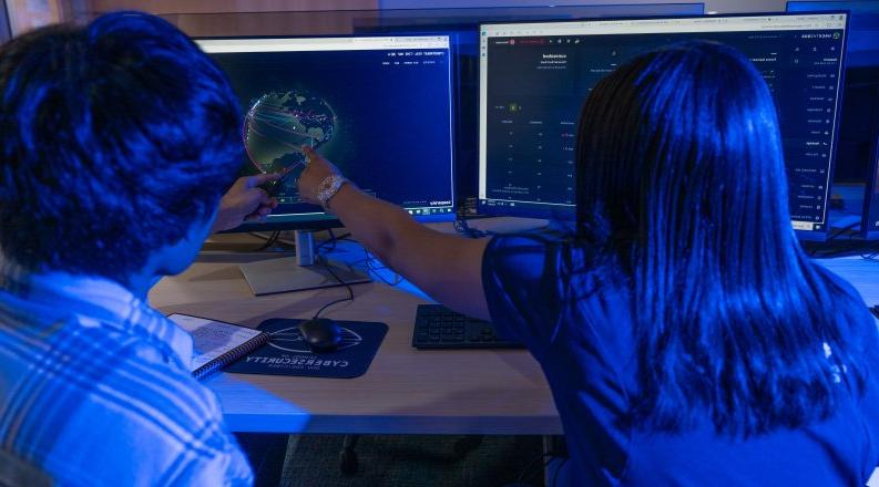 Two students in a computer lab look at an image of a global map.