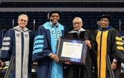 Four men pose for a photo with a framed college degree.